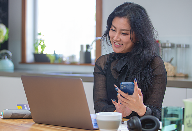 A young woman in a black shirt completes yet another two-factor authentication task on her smartphone so that she may access content on her laptop.