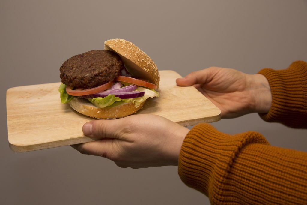 Burger with vegetarian patty on wooden board, held by  2 hands